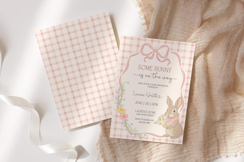 Op de afbeelding: Een uitnodiging voor een babyshower met een roze ruitpatroon en de tekst "Some Bunny is on the Way". De uitnodiging toont een cartoonkonijn met bloemen en een decoratieve bloemenrand. De uitnodiging is ongeveer 13 x 18 cm groot.