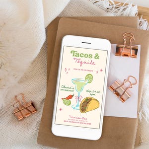 May include: A smartphone displays a party invitation with the text "Tacos & Tequila." The invitation features illustrations of a margarita, a taco, and a chili pepper. The phone rests on a stack of brown paper with rose gold binder clips.