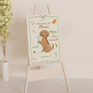 May include: A rectangular sign featuring a brown dachshund holding a martini glass, with text reading Welcome to Olivia's Weenies & 'Tinis Bachelorette, Aug 2026, Olive Hill, CA, surrounded by illustrations of hot dogs, olives, and martini glasses.