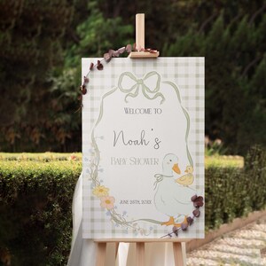 Pu&ograve; includere: Un cartello di benvenuto per una baby shower in gingham verde e bianco con una ghirlanda di fiori, un fiocco e un cartone animato di un'anatra e un anatroccolo. Il cartello dice "Benvenuti alla baby shower di Noah" e "26 giugno 20XX".