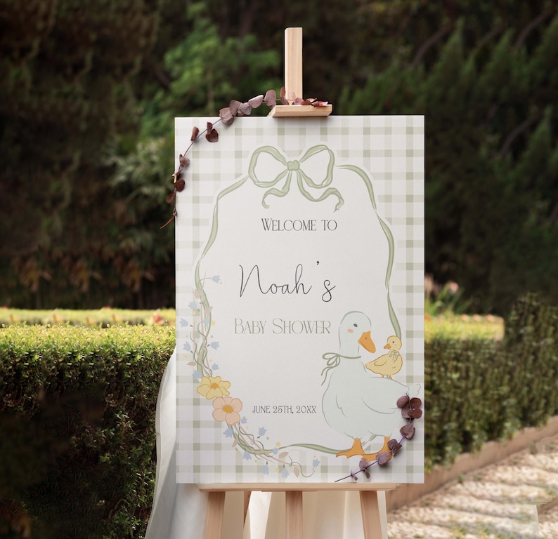 Pu&ograve; includere: Un cartello di benvenuto per una baby shower in gingham verde e bianco con una ghirlanda di fiori, un fiocco e un cartone animato di un'anatra e un anatroccolo. Il cartello dice "Benvenuti alla baby shower di Noah" e "26 giugno 20XX".