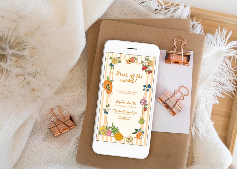 May include: A white smartphone displaying a digital invitation with a light orange striped background, decorated with colorful illustrations of various fruits and flowers, featuring the text Fresh off the market, Sophie Smith, and event details.