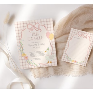 May include: Two pink and white gingham patterned cards with a floral design. The larger card has a pink bow and the text "Time Capsule To Celebrate [Name]'s 1st Birthday!" The smaller card has a blank space for writing.