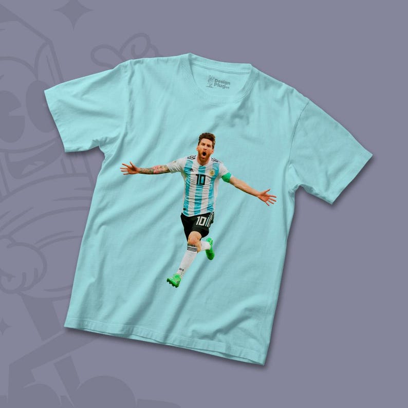 Peut inclure: Un t-shirt bleu clair avec un motif repr&eacute;sentant un joueur de football portant un maillot bleu et blanc avec le num&eacute;ro 10. Le joueur est en l'air, les bras tendus, c&eacute;l&eacute;brant un but.