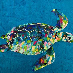 Puede incluir: Un diseño de tortuga marina de patchwork colorido sobre un fondo azul. La tortuga está hecha de varios retazos de tela en tonos de azul, verde, rosa y naranja. Se ven la cabeza y las aletas de la tortuga, con un ojo detallado.