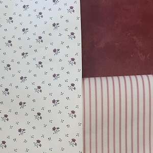 May include: Two rolls of wallpaper, one with a white background and a small red floral pattern, and the other with a white background and thin red stripes.