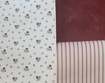 May include: Two rolls of wallpaper, one with a white background and a small red floral pattern, and the other with a white background and thin red stripes.