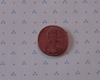 May include: A close-up of a white wallpaper with a repeating pattern of small blue triangles and red dots. A penny is placed in the centre of the image.