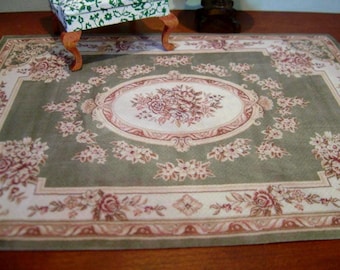 May include: A green and cream patterned rug with a floral design. The rug has a central oval medallion with a floral design in shades of pink and cream.