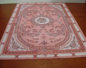 May include: A pink and white patterned rug with a floral design. The rug has a border with a repeating pattern.