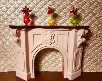 May include: A pink painted miniature fireplace with a decorative carved design above the archway. Three small vases with red, yellow, and green glass are on the mantel.
