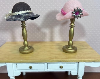 May include: Two miniature hats on display stands. The hat on the left is brown with a white ribbon and the hat on the right is pink with a pink ribbon and a silver star with a pink jewel.