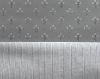 May include: A close-up of two pieces of fabric. The top piece is a light grey fabric with a repeating pattern of white stylised flowers. The bottom piece is a white fabric with a vertical ribbed texture.