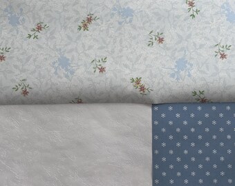 May include: A close-up of two different patterned fabrics. The top fabric is a light blue with a small floral pattern. The bottom fabric is a white fabric with a textured surface and a blue fabric with a small white dot pattern.