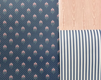 May include: A close-up of three different patterned wallpaper samples. The first sample is a dark blue wallpaper with a repeating pattern of pink and green flowers. The second sample is a light pink wallpaper with a wood grain texture. The third sample is a white and blue striped wallpaper.