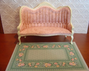 May include: A white and pink upholstered loveseat with a floral patterned rug underneath. The loveseat has a curved back and ornate legs.