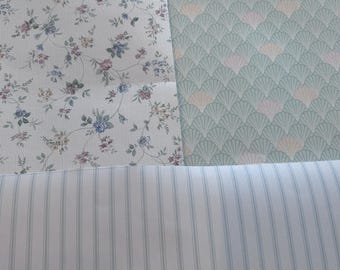 May include: Three different patterns of fabric swatches. The top left swatch is a white fabric with a floral pattern in shades of pink, blue, and green. The top right swatch is a green fabric with a repeating pattern of light green and pink fan shapes. The bottom swatch is a white fabric with thin blue stripes.