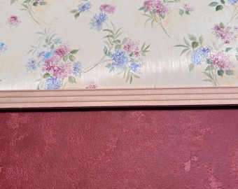 May include: A close-up of a wall with a floral wallpaper pattern featuring pink and blue flowers on a cream background. The wallpaper is topped with a wooden trim and a solid red wall below.
