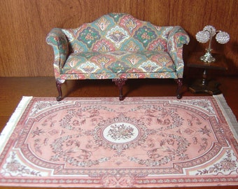 May include: A pink and white patterned rug with a floral design. A small, floral patterned sofa sits on the rug with a small table and lamp beside it.