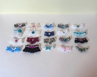 May include: A collection of 18 delicate lace garters in various colors and patterns, including white, blue, pink, black, and red. Some garters feature embellishments like rhinestones, beads, and flowers.