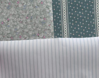 May include: A close-up of three fabric swatches. The top swatch is a green fabric with a floral pattern. The middle swatch is a green fabric with a white and blue geometric pattern. The bottom swatch is a white fabric with thin blue stripes.