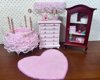 May include: A miniature nursery scene with a pink crib, dresser, and heart-shaped rug. The crib has a ruffled lace skirt. A small cabinet is filled with miniature items. A teddy bear sits on the dresser.
