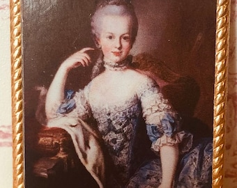 May include: Miniature portrait of a woman in a blue dress with white lace trim, set in a gold-colored frame. The painting depicts a woman with powdered hair, resting her arm on a chair. The frame has a rope-like design.