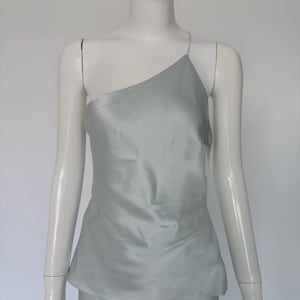 Könnte beinhalten: Ein hellgrünes One-Shoulder-Top aus seidigem Material. Das Top hat ein schlichtes Design mit einem einzelnen Spaghettiträger. Der Stoff hat einen subtilen Glanz, der ihm ein luxuriöses Aussehen verleiht. Das Oberteil wird auf einer Schaufensterpuppe präsentiert.