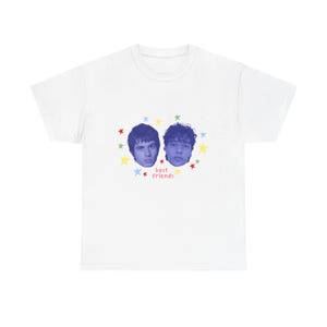 Könnte beinhalten: Weißes T-Shirt mit einer Grafik von zwei Gesichtern mit blauen Hauttönen, umgeben von bunten Sternen. Die Worte "best friends" sind darunter gedruckt. Ein lässiges und lustiges Design.