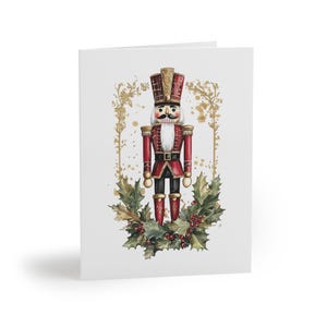 Peut inclure: Carte de vœux de Noël avec une illustration à l'aquarelle d'un soldat casse-noisette traditionnel. Le casse-noisette porte un uniforme rouge avec des détails dorés, un grand chapeau et une barbe blanche. Le design comprend du houx et des baies.