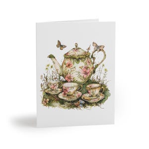 May include: A greeting card featuring a watercolor illustration of a tea set. The set includes a teapot and three teacups with saucers, all adorned with pink floral patterns. Butterflies and wildflowers add to the whimsical design.