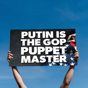 Puede incluir: Un cartel con el texto "PUTIN IS THE GOP PUPPET MASTER" en letras blancas sobre un fondo negro. El cartel se sostiene contra un cielo azul, con una parte de la bandera estadounidense visible.