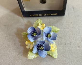 May include: A blue and white porcelain flower brooch with green leaves. The brooch is in its original box, which reads "Hilvercastle Florals English Bone China Made in England".