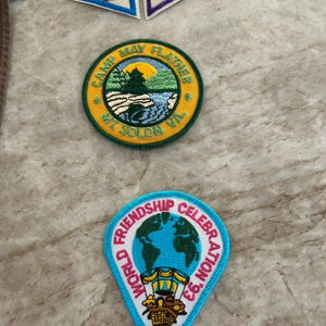May include: A collection of embroidered patches. Includes two triangular patches with nature scenes and a round patch with "Camp May Flather Mt. Solon VA" text and a landscape. A blue and white patch reads "World Friendship Celebration '93".