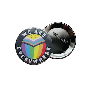 May include: A black button with a rainbow and the text "We are everywhere" in white. The button has a safety pin on the back.
