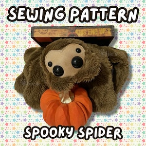 May include: A brown plush spider toy with a tan face and multiple black eyes, holding a bright orange fabric pumpkin. The text SEWING PATTERN and SPOOKY SPIDER are printed in white letters with black outlines above and below the plush toy.