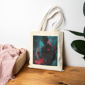 May include: A cream-colored tote bag featuring a digital art print. The artwork depicts a silhouetted figure in a top hat, with red and teal accents. The figure is holding a small object, set against a swirling, cosmic background.