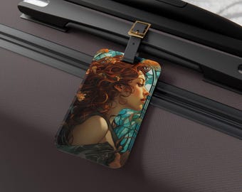 May include: A rectangular luggage tag featuring an artistic illustration of a woman with long, red hair. The tag has a black leather strap with a gold-colored buckle. The artwork has a teal and blue background.