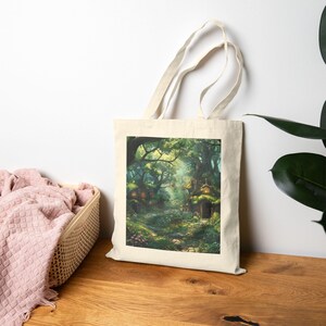 May include: A cream-coloured tote bag displaying a detailed illustration of a magical forest. The artwork shows quaint dwellings hidden amongst verdant foliage, with a winding path. The bag has long handles and a simple design. The scene is full of light.
