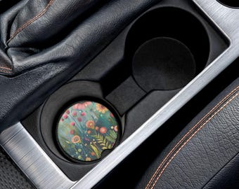 Könnte beinhalten: Ein floraler Auto-Untersetzer mit einem Aquarelldesign aus rosa, orangefarbenen und gelben Blumen auf türkisfarbenem Hintergrund. Der Untersetzer befindet sich in einem schwarzen Auto-Getränkehalter, umgeben von schwarzem Leder und silbernen Zierleisten.