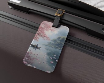 May include: A rectangular luggage tag featuring a serene landscape with a boat on a lake, cherry blossoms, and a person in the boat. The tag is attached to a black suitcase handle with a gold buckle.