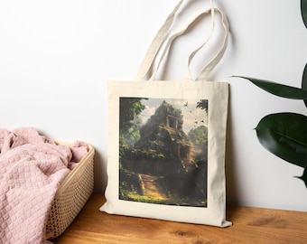 May include: A beige tote bag featuring a detailed illustration of an ancient temple in a lush, green jungle. The artwork depicts a stone structure with steps, surrounded by trees and birds. The bag has long handles and is displayed on a wooden surface.