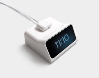 Op de afbeelding: Een wit oplaadstation met een wit draadloos oplaadpad en een witte telefoonhouder. De telefoonhouder heeft een zwart scherm waarop de tijd 11:10 wordt weergegeven.