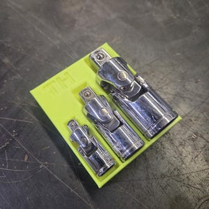 May include: Three chrome universal joint sockets of different sizes are displayed on a bright yellow holder. The holder has the letters "TH" printed on it. The tools are set against a dark, textured surface.