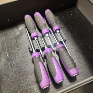 May include: A set of six screwdrivers with black and purple handles, neatly arranged in a drawer. The handles are a combination of black and purple, with the size of the screwdriver printed on the handle. The tools are designed for various mechanical tasks.