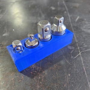 May include: A set of four silver metal socket adapters of varying sizes, held in a bright blue plastic holder. The adapters are designed for use with a wrench or other tools. The holder keeps the adapters organized.