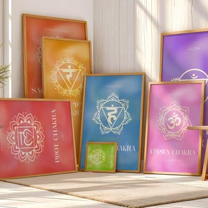 May include: A collection of framed chakra art prints in various sizes. Each print features a gradient background and a white chakra symbol with text. The frames are a light wood color, and the prints are displayed on a neutral rug.