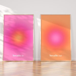 Peut inclure: Deux affiches encadrées avec un design en dégradé. L'une est rose avec le texte "breathe in", l'autre est orange avec le texte "breathe out". Les affiches ont un effet doux et flou et sont exposées sur un sol en bois.