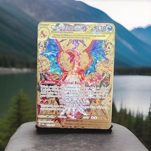May include: A gold Charizard EX Pokémon card featuring a red and orange dragon with blue wings. The card has the text "Charizard EX" and "Burning Darkness 180+". The card is set against a scenic background.