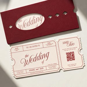 Peut inclure: Une pochette en papier rouge foncé avec une découpe ovale et des formes en losange, accompagnée d'une invitation de mariage style ticket couleur crème. Le carton présente du texte rouge, un QR code et les noms Annabel et Jason.